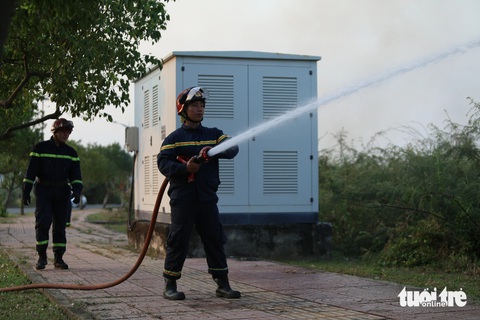 Cháy cỏ trong khu công nghệ cao, bụi than bay tới làng đại học- Ảnh 3. Lực lượng cảnh sát PCCC có mặt phun nước xung quanh tủ điện để tránh lửa bén vào - Ảnh: MINH HÒA