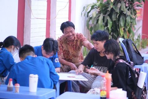 Sinh viên vẽ bảng hiệu miễn phí cho người buôn bán khó khăn- Ảnh 1. Chú Nguyễn Bá Quý ngồi trò chuyện cùng các bạn sinh viên trong lúc các bạn đang vẽ bảng hiệu. Chú cho biết cứ tưởng mấy đứa nói chơi, ai ngờ làm thiệt - Ảnh: NGỌC PHƯỢNG