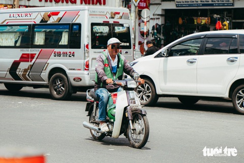 Một người mặc áo shipper dù có nón bảo hiểm nhưng lại treo trên xe chứ không đội lên đầu - Ảnh: THANH HIỆP Một người mặc áo shipper dù có mũ bảo hiểm nhưng lại treo trên xe chứ không đội lên đầu - Ảnh: THANH HIỆP