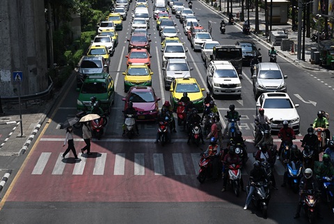 Thái Lan cảnh báo nắng nóng nguy hiểm ở Bangkok và nhiều tỉnh thành- Ảnh 1. Người đi bộ mang ô qua đường trong khi người đi xe máy chờ dưới bóng râm để tránh nắng ở Bangkok, Thái Lan trong ảnh chụp đầu tháng 4 - Ảnh: AFP