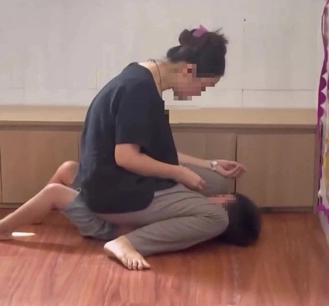 Bạo lực do vô minh- Ảnh 1. Chủ nhóm lớp mầm non đè cháu trai xuống, ngồi hẳn lên người rồi nhét thức ăn vào miệng cháu - Ảnh: Cắt từ video