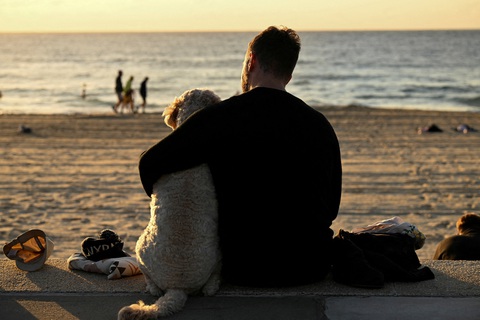 Một người đàn ông quàng tay ôm con chó của mình khi ngồi trên bãi biển ở Coogee tại thành phố Sydney, bang New South Wales, Úc vào ngày 25-4 - ẢNH: REUTERS Một người đàn ông quàng tay ôm con chó của mình khi ngồi trên bãi biển ở Coogee tại thành phố Sydney, bang New South Wales, Úc vào ngày 25-4 - ẢNH: REUTERS
