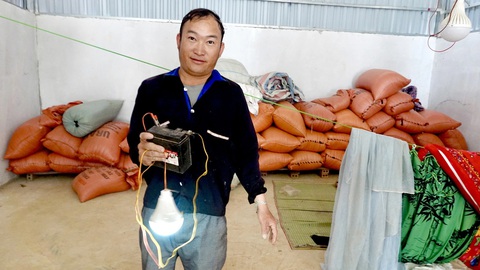 Ân tình trên đất Điện Biên - Kỳ cuối: Sáng điện ở Điện Biên Đông- Ảnh 1. Anh Vừ A Súa ở Huổi Tấu phải dùng ắc quy sạc để bật bóng đèn khi cả nhà ăn tối - Ảnh: NGỌC QUANG