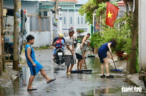 Mưa mới 15 phút, rác từ rạch trồi lên đầy đường Tô Ngọc Vân, TP Thủ Đức- Ảnh 6. Người dân tại các con hẻm lân cận hì hục dọn rác, đẩy nước từ rạch tràn lên - Ảnh: CHÂU TUẤN