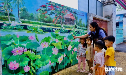 Hàng trăm tranh bích họa sen hưởng ứng Lễ hội sen Đồng Tháp- Ảnh 1. Cô giáo hướng dẫn các bé xem tranh bích họa sen Trường mầm non Hồng Gấm, TP Cao Lãnh - Ảnh: ĐẶNG TUYẾT