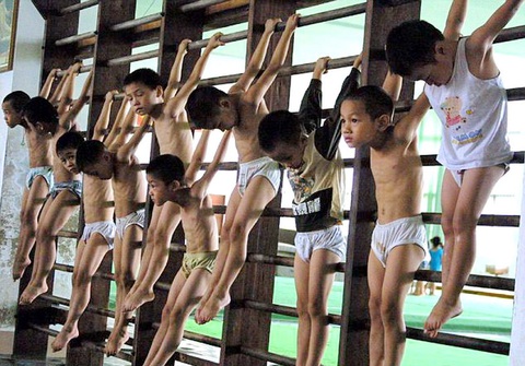 Gian nan cuộc đời những vận động viên thể dục dụng cụ- Ảnh 1. Những vận động viên thể dục dụng cụ nhí ở Trung Quốc phải làm quen với xà ngang từ nhỏ theo cách này - Ảnh: BARCROFT MEDIA