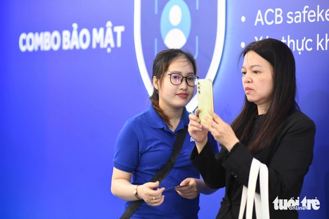 Chăm chú học cách bảo vệ tài khoản ngân hàng tại Lễ hội Không tiền mặt- Ảnh 3. Chị Thùy Vân (trái) chăm chú làm theo hướng dẫn của nhân viên ACB để xác thực khuôn mặt, tăng cường đảm bảo an toàn trong tài khoản - Ảnh: QUANG ĐỊNH