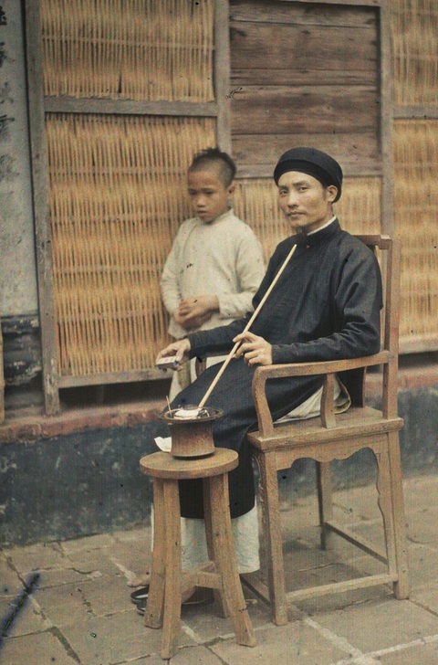 Ông lý trưởng hút thuốc lào trên sân nhà. Ảnh: Léon Busy. Ông lý trưởng hút thuốc lào trên sân nhà - Ảnh: Léon Busy