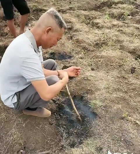 Thực hư mặt ruộng 'tự bốc cháy' kỳ lạ ở cánh đồng Gia Lai- Ảnh 1. Người đàn ông dùng que chọt xuống mô đất đang bốc khói trên cánh đồng xã Bar Măih, huyện Chư Sê, Gia Lai - Ảnh: TikTok