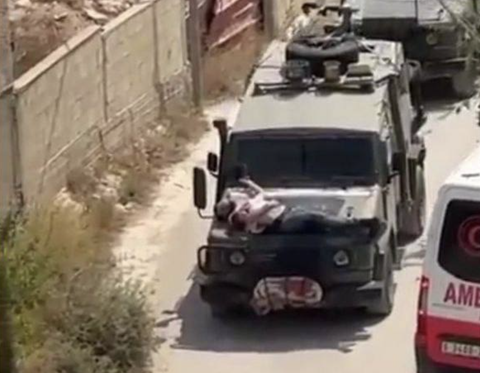 Ảnh chụp màn hình đoạn clip cho thấy một người đàn ông Palestine bị trói vào mui một xe quân sự Israel Ảnh chụp màn hình đoạn clip cho thấy một người đàn ông Palestine bị trói vào mui một xe quân sự Israel