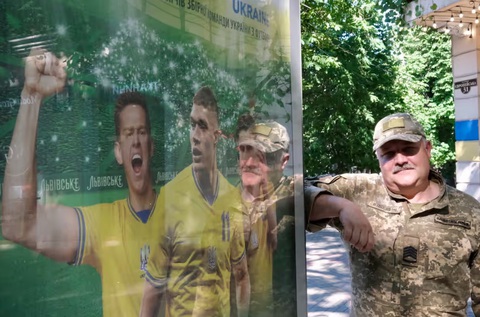 Mặc kệ chiến tranh, người dân Ukraine hòa vào không khí Euro 2024- Ảnh 7. Một người lính đứng dựa vào biển quảng cáo Euro 2024 tại thành phố cảng Odessa, Ukraine. Đây là một trong số ít biển quảng cáo về Euro 2024 tại đường phố Odessa, vì chiến tranh gần như đã chiếm toàn bộ các thông điệp tuyên truyền trên phố - Ảnh: RICHARD MORGAN