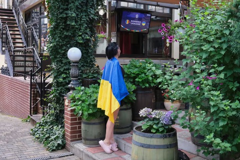 Mặc kệ chiến tranh, người dân Ukraine hòa vào không khí Euro 2024- Ảnh 9. Một cô gái Ukraine đang khoác quốc kỳ lên người và háo hức chờ đợi trận đấu giữa Ukraine và Romania. Trên quốc kỳ, cô viết to cụm từ “Kherson” - tên một thành phố ở Ukraine và cũng là quê hương của cô. Tuy nhiên, cô gái này đã phải ly hương trước các cuộc không kích của Nga - Ảnh: RICHARD MORGAN