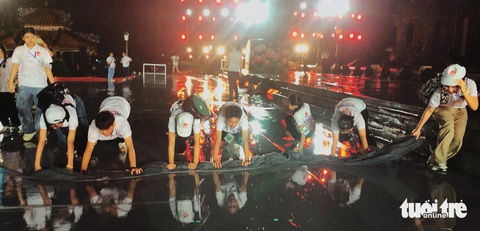 Bạn trẻ đội mưa lau sân khấu, phục vụ lễ khai mạc Festival Huế 2024- Ảnh 3. Các tình nguyện viên cùng nhau khom lưng đẩy nước và làm khô sân khấu - Ảnh: BẢO PHÚ