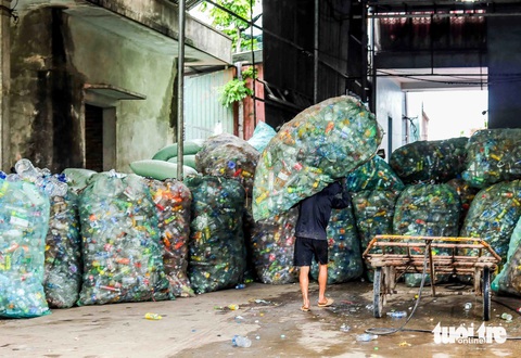Mưu sinh ở Một người đàn ông làm ở xưởng xay vác trên lưng bao tải phế liệu để tập kết vào nhà kho - Ảnh: THÚY TRANG