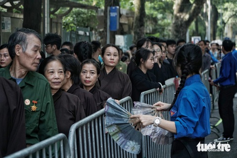 Tay liên tục phẩy mạnh quạt về phía người dân, Nguyệt nói: “Hôm nay trời rất nóng, người xếp hàng đông nên chúng em đã quyết định dùng quạt tay cho người dân để dân đỡ mệt. Mọi người đến đây còn sớm hơn chúng em, từ 3-4 sáng đã tới để xếp hàng. Với lại được phục vụ trong tang lễ của Tổng Bí thư Nguyễn Phú Trọng là niềm tự hào của em. Hôm nay chúng em nhận được rất nhiều lời cảm ơn của người dân Người dân xếp quạt cây ra đường, pha nước chanh cho người đến viếng Tổng Bí thư Nguyễn Phú Trọng- Ảnh 11.