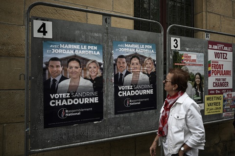 Ông Macron vắng bóng trước công chúng gần 2 tuần- Ảnh 2. Một cử tri Pháp đứng bên cạnh hình ảnh của các ứng cử viên RN trong chiến dịch bầu cử ngày 2-7 - Ảnh: AFP