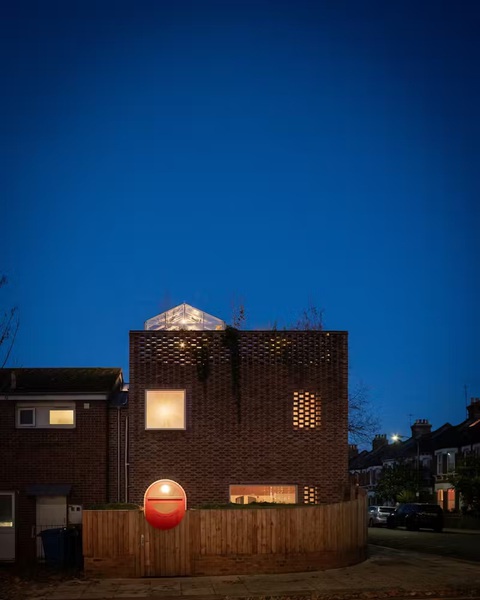 Ngôi nhà bằng gạch thủ công - điểm nhấn lạ lùng ở Peckham, London- Ảnh 4. Ngôi nhà với khung cửa ra vào màu đỏ trong ánh đèn đêm - Ảnh: dwell