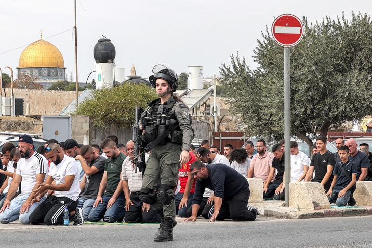 Quân nhân Israel đi ngang qua những tín đồ Hồi giáo đang cầu nguyện ở núi Ô-liu, đông Jerusalem, vào ngày 27-10, diễn ra trước cuộc tuần hành thể hiện đoàn kết với người dân Palestine ở Dải Gaza - Ảnh: AFP