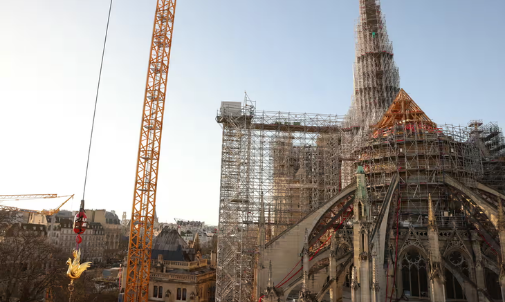 Chú gà trống vàng mới (góc trái) đang được đưa lên nóc nhà thờ Đức Bà Paris - Ảnh: AFP