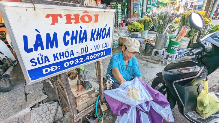 Không có chỗ làm việc, ông Thôi ngồi bệt xuống đất để sửa dù cho khách   - Ảnh: NHẬT LINH