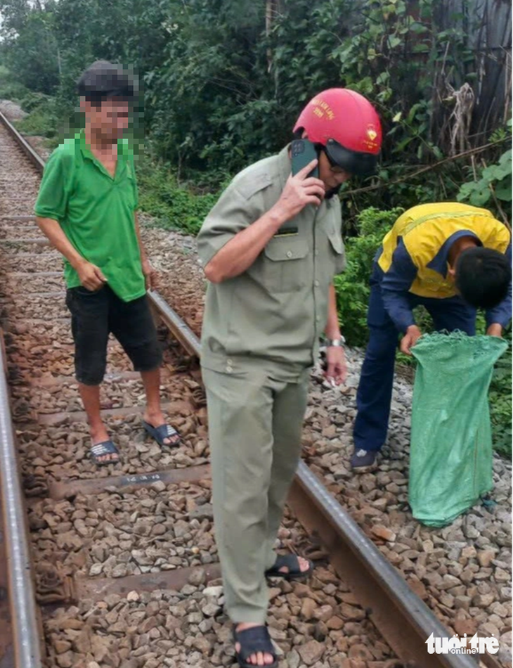 Người đàn ông (mặc áo xanh, đứng bên trái) tháo trộm ốc, vật tư trên đường ray - Ảnh: CTV