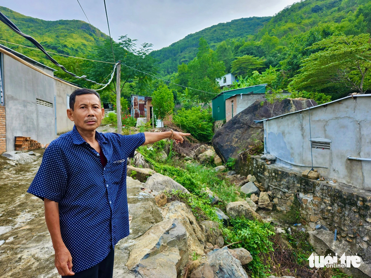 Ông Lê Văn Sửu chỉ tay về phía con suối nơi chứa đầy đá sau vụ sạt lở - Ảnh: MINH CHIẾN