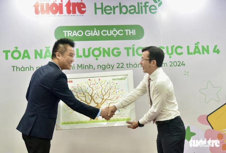 Giám đốc truyền thông Herbalife Việt Nam Nguyễn Thành Đạt (bên trái) nhận bức tranh có dấu vân tay của tất cả khách mời mang thông điệp lan tỏa lối sống tích cực từ tay Phó tổng biên tập báo Tuổi Trẻ Trần Xuân Toàn - Ảnh: T.T.D.