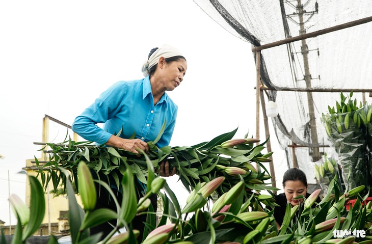 Bà Vinh bận rộn cắt hoa, bó hoa cho khách, còn chồng bà tiếp khách buôn, khách lẻ cả ngày - Ảnh: NGUYỄN HIỀN