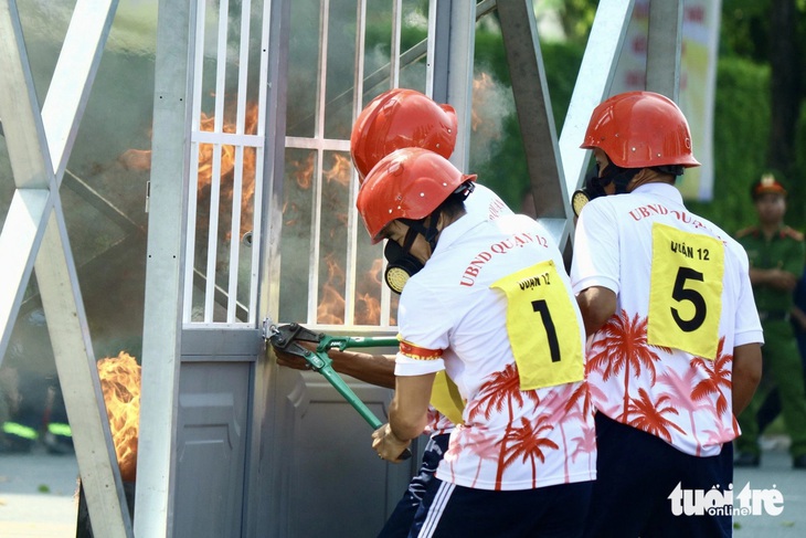 Các thí sinh dùng kềm phá khóa để vào trong căn nhà (mô hình) đang bốc cháy dập lửa - Ảnh: KHẮC HIẾU