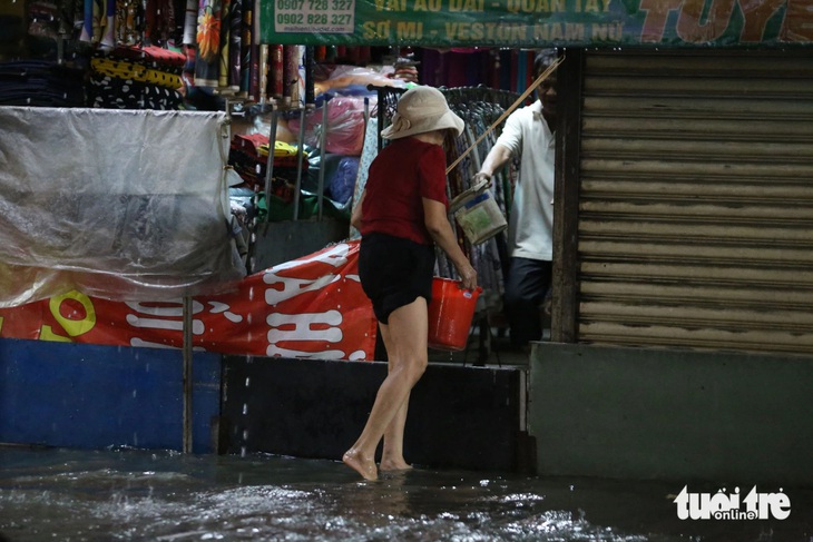 Bà Kim, bán hàng ở chợ Thủ Đức, dùng tấm gỗ che chắn nhưng nước vẫn tràn vào chỗ buôn bán. Bà Kim phải hì hục tát nước mỗi khi mưa ngập - Ảnh: MINH HÒA