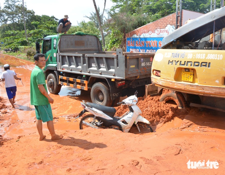 Người dân đang chờ được kéo xe máy lên dưới lớp bùn cát đỏ - Ảnh: ĐỨC TRONG