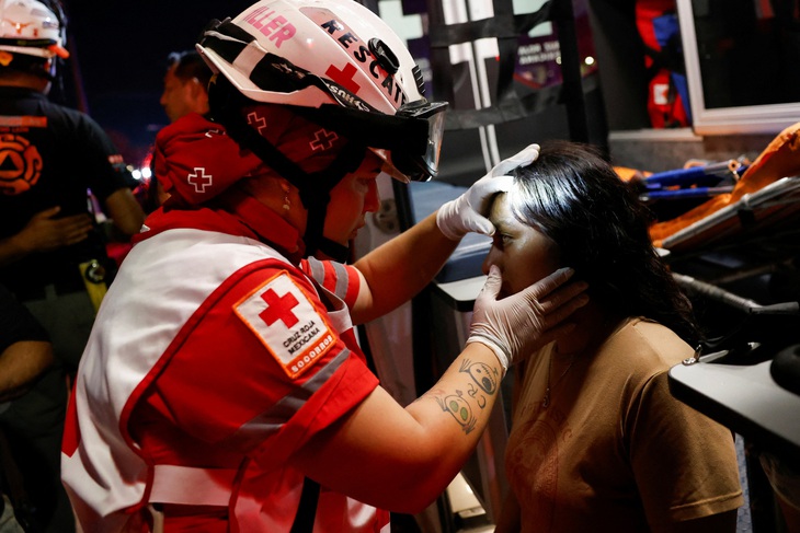 Nhân viên của Hội Chữ thập đỏ Mexico đang kiểm tra mắt cho một cô gái sau vụ tai nạn - Ảnh: REUTERS