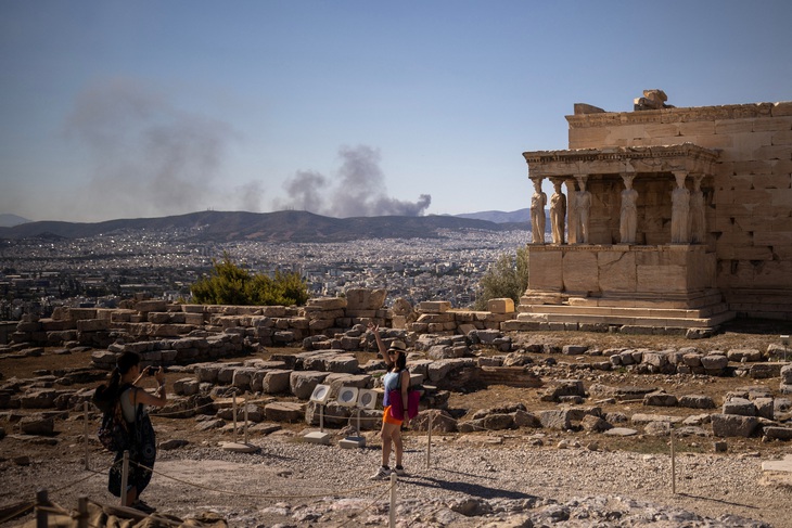 Một khách du lịch tạo dáng chụp ảnh trên đỉnh đồi Acropolis, phía sau là một đám cháy, giữa nhiệt độ cao ở Athens, Hy Lạp hôm 16-7 - Ảnh: REUTERS