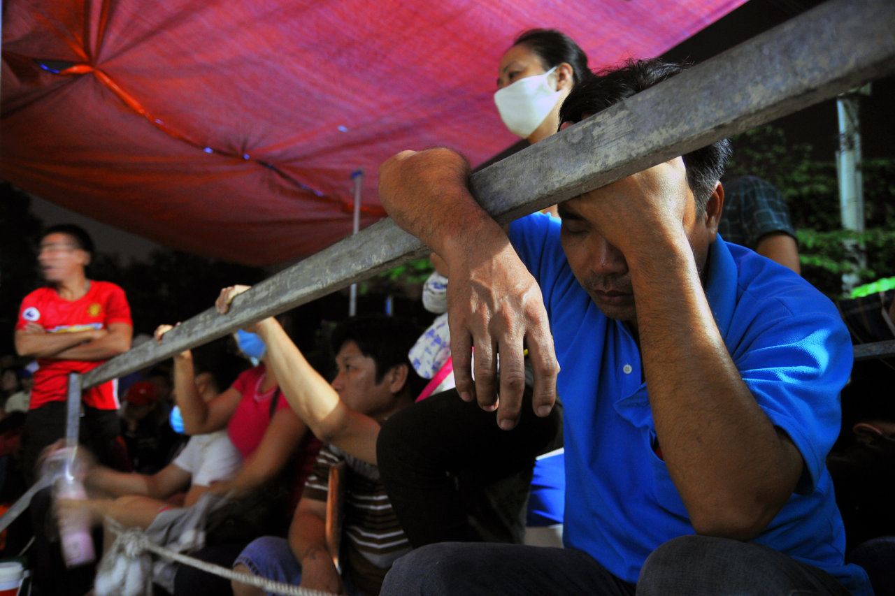 A parent rests against the metal fence for a quick nap. Photo: Tuoi Tre