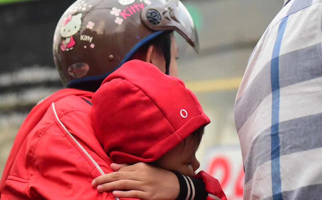 A woman holds her child on the back of a motorcycle.