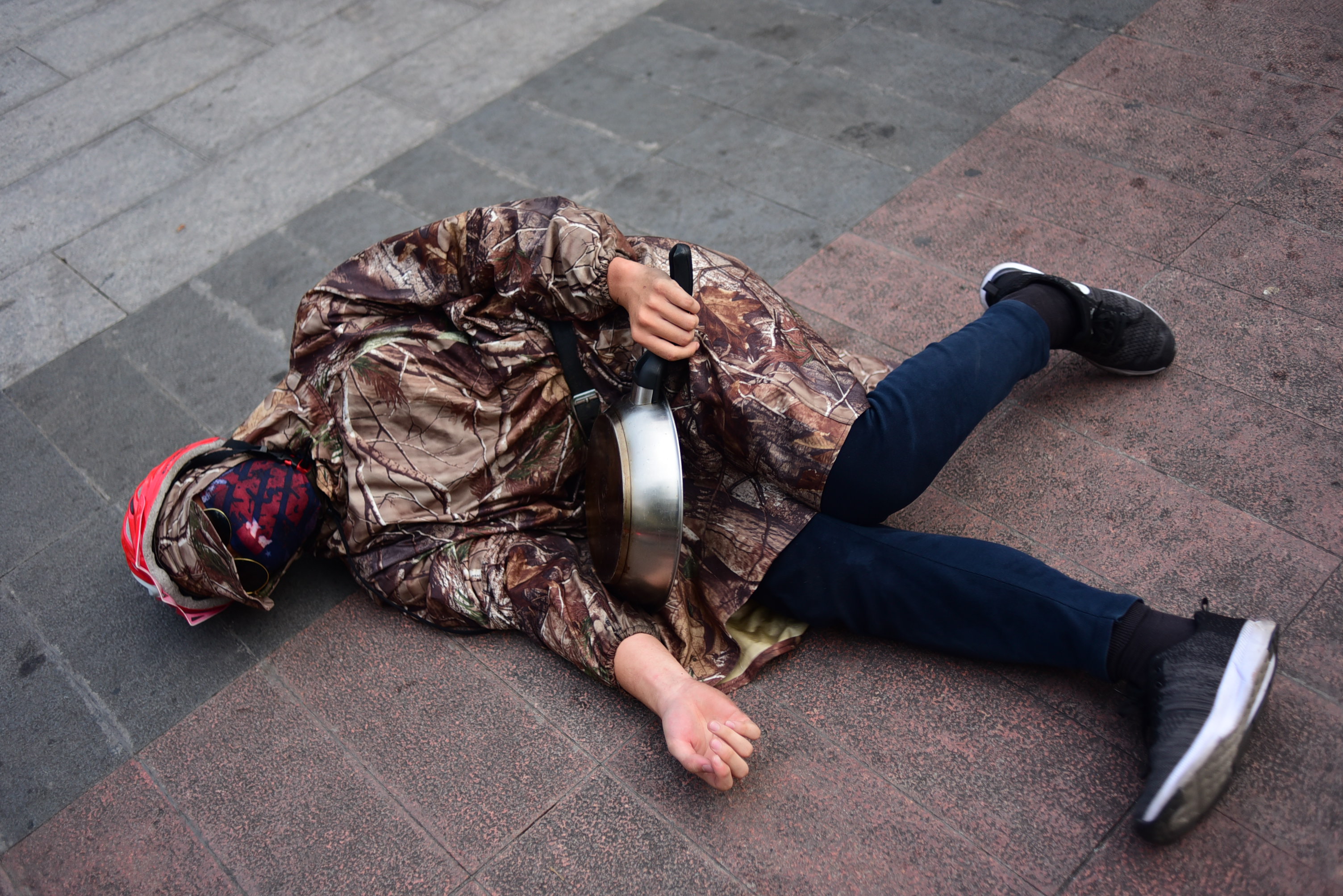 A boy performs a unique pose with his pan on the ground.