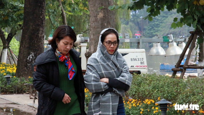 A woman wraps her head and torso with a scarf to keep warm.