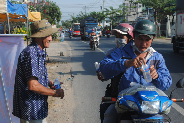 Nguyen Van Thanh talks with a woman who is holding a water bottle he has given along road crossing Dong Thap Province, southern Vietnam, January 30, 2019. Photo: Thanh Nhon / Tuoi Tre