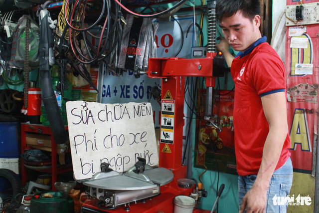 A mechanic stands beside a sign saying motorbike repair was offered free of charge during a rainstorm in Da Nang in December 2018. Photo: Doan Nhan / Tuoi Tre