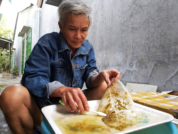 Vo Ngoc Hung uses a tooth brush to lightly scratch off the green layer of the almond leaves after being chemically treated. Photo: An Nhien / Tuoi Tre