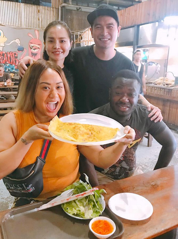 Pham Thanh Danh poses for a photo with foreign tourists who have Vietnamese pancake (banh xeo) at his diner in Ho Chi Minh City. Photo: Quoc Linh / Tuoi Tre