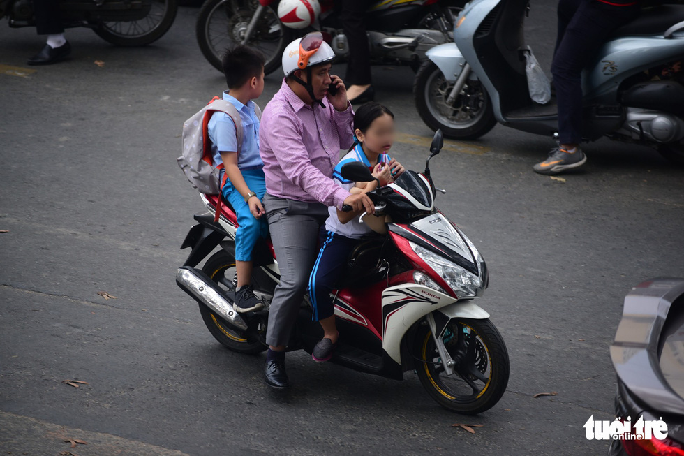 A man carries two children, who wear no helmet, on Nguyen Thi Minh Khai Street in District 3, in Ho Chi Minh City. Photo: Quang Dinh / Tuoi Tre