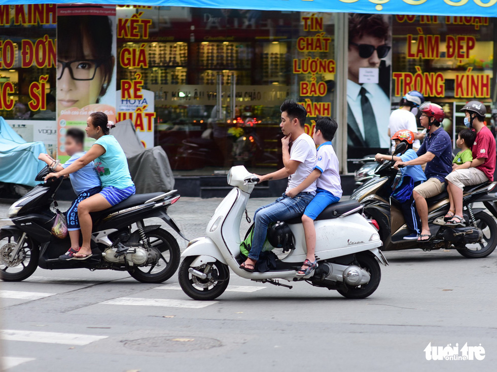 A man carries his child on a motorbike on Tran Quang Khai Street in Ho Chi Minh City, with helmets being hung on the vehicle instead of being worn by the two. Photo: Quang Dinh / Tuoi Tre