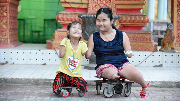 Thuong and Thao smile for a photo on special wheelchairs made by Thuong’s father. Photo: Tu Trung / Tuoi Tre