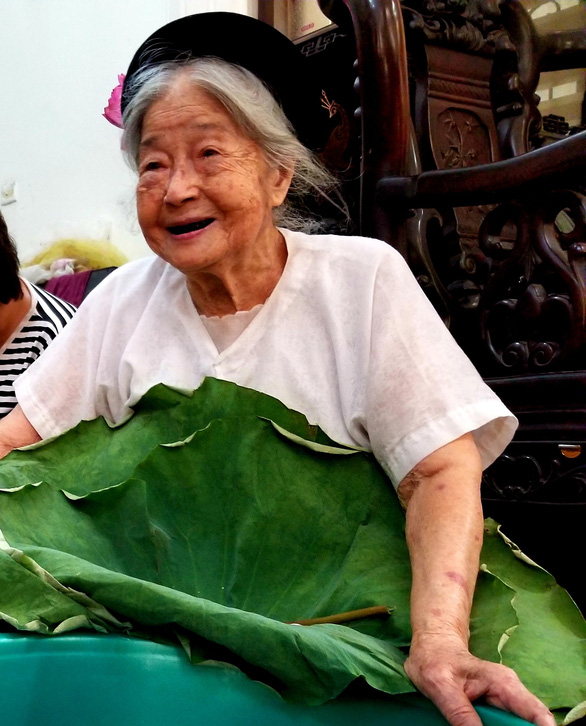 95-year-old Nguyen Thi Dan smiles for a photo while holding a big lotus leaf. Photo: Ha Thanh / Tuoi Tre