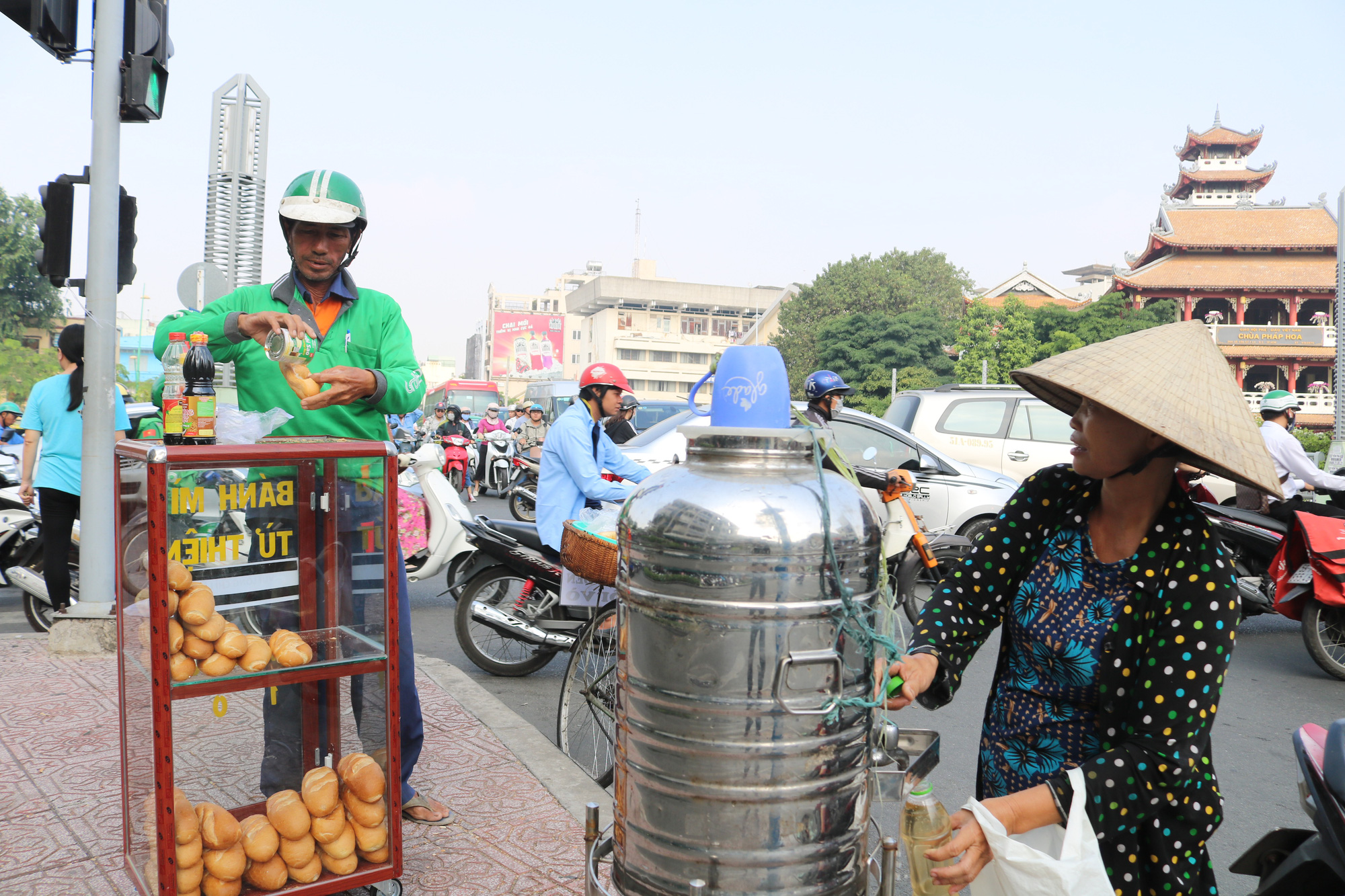 A man prepares a bread as a woman fills her bottle with iced tea at a free bread box donated by college student Nguyen Thi My Dung in Ho Chi Minh City. Photo: Ngoc Phuong / Tuoi Tre
