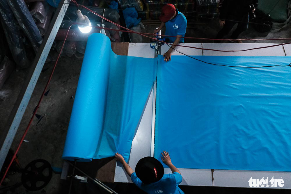 Two workers cut a piece of fabric to make face masks at a raincoat factory in Dong Anh District, Hanoi, Vietnam. Photo: Mai Thuong / Tuoi Tre