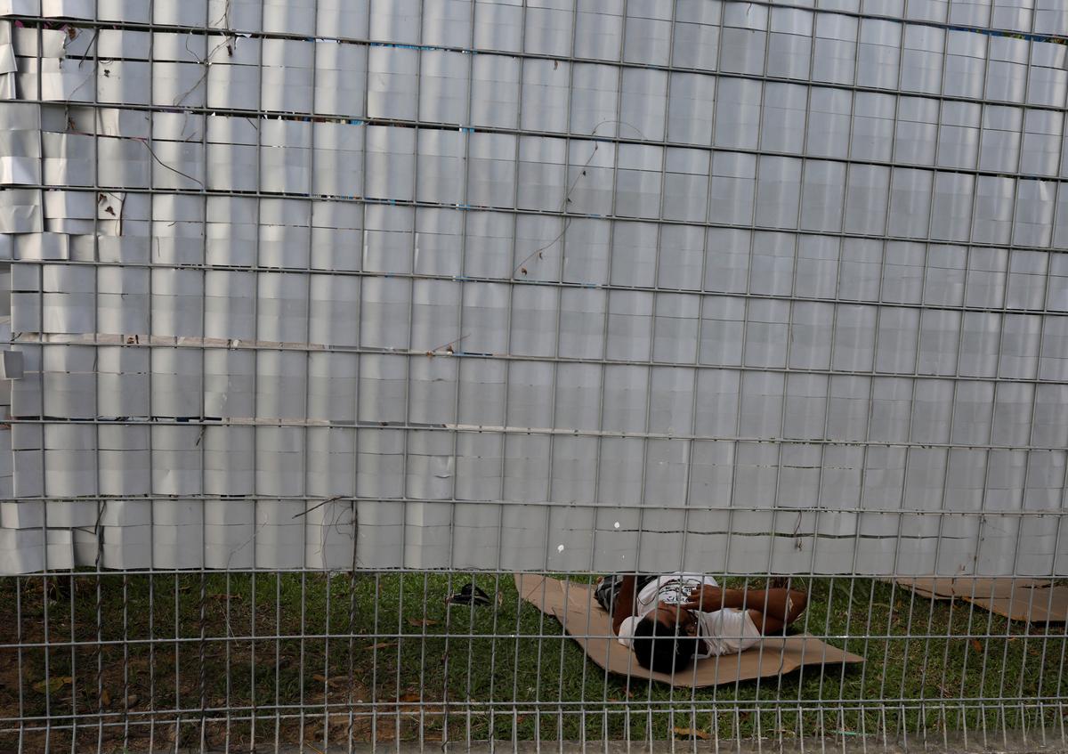 FILE PHOTO: A migrant worker rests on the ground behind the fence of the Punggol S11 dormitory during the coronavirus outbreak (COVID-19) in Singapore April 6, 2020.  Photo: Reuters