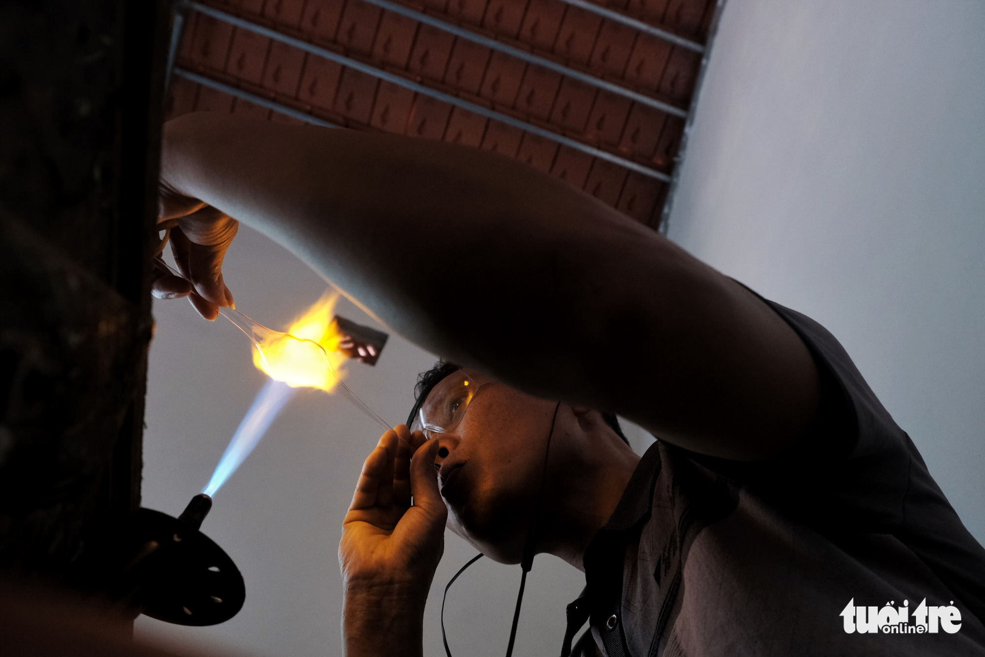 A glass blowing artist mixes a blob of molten glass with the end of a long pipe and blows air into the other end, which makes the blob swell. Photo: Mai Thuong / Tuoi Tre