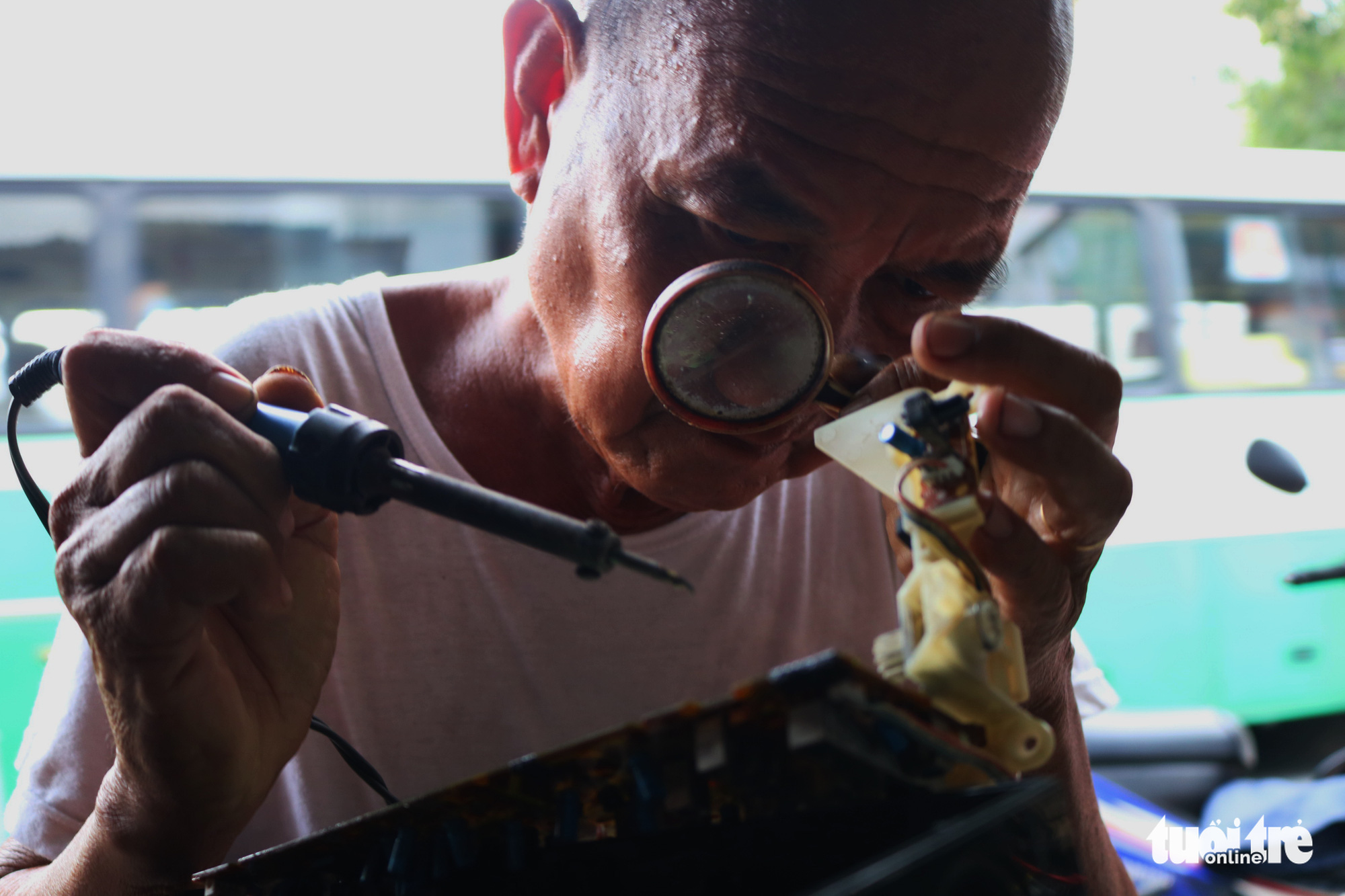Tran Minh Tri uses a magnifying glass to solder a circuit board at the radio repair shop on Vo Van Ngan Street in Thu Duc District, Ho Chi Minh City. Photo: Hoang An / Tuoi Tre